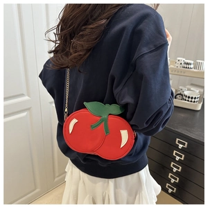 Detail view of red cherry shaped shoulder bag with green leaf and metal chain on a model