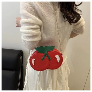 Red cherry shaped shoulder bag with leaf detail and gold chain shown on a model