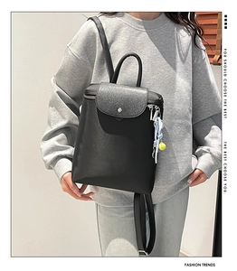 Close-up of minimalist black backpack with textured lid and neon yellow tennis ball charm