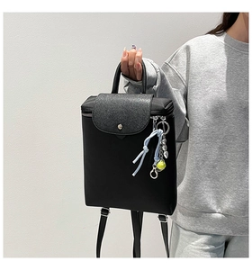 Detail of black nylon backpack with leather flap and vibrant tennis ball keychain accessory