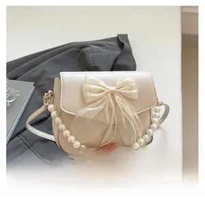 Detailed macro view of cream beige shoulder bag featuring a large mesh bow and pearl strap