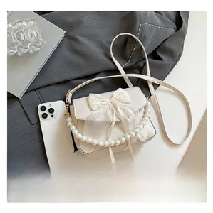 Detail of cream white crossbody bag featuring a mesh bow and pearl chain handle