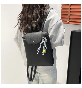 Detail of black faux leather backpack with tennis ball charm on model back in room