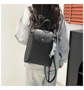 Detail of minimalist black backpack with leather flap and blue charm on model