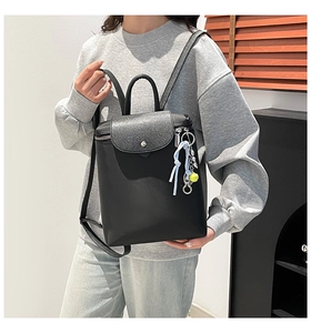Detail of black leather backpack featuring grainy texture flap and tennis ball charm