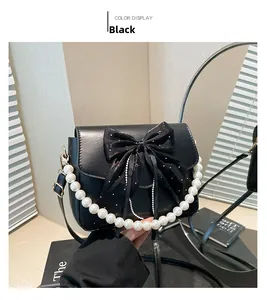 Detail of black bow shoulder bag with white polka dots and elegant pearl handle strap