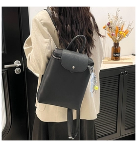 Close-up of a minimalist black leather backpack with a flap cover and tennis ball charm