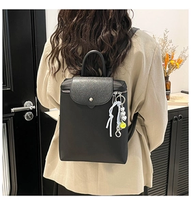 Detail of minimalist black backpack with flap snap button and decorative side pendant
