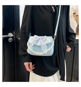 Detail of light blue crossbody bag featuring a translucent bow and pearl chain strap