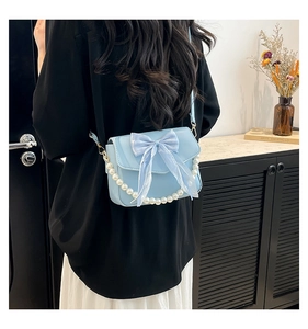Detail of light blue crossbody bag featuring a mesh bow and pearl chain decoration