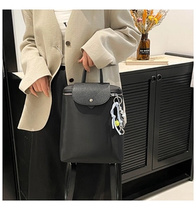 Detail of black minimalist backpack with pebble texture flap and sporty pendant accessory