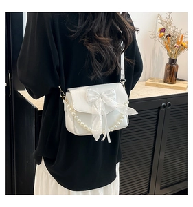 Detailed view of white crossbody bag featuring a large bow and pearl chain on back strap