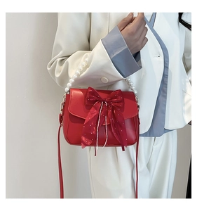 Detail of red bow shoulder bag featuring a large mesh knot and elegant pearl handle