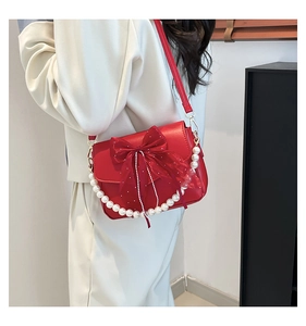 Detail of red bow knot handbag with pearl chain strap worn by a model in a stylish setting