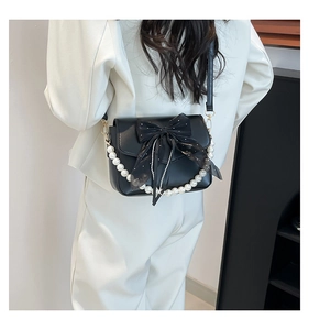 Detail of black leather crossbody bag with mesh bow and large pearl chain accessory
