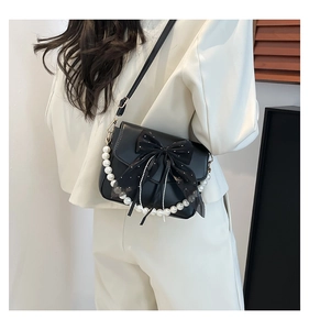 Detail of black leather crossbody bag with sheer bow and pearl chain on a white blazer