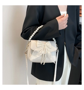 Detail of cream white underarm bag with a sheer gauze bow and elegant pearl tassel decor