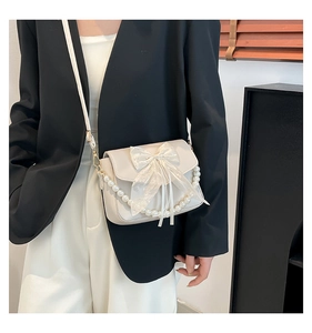 Detailed view of cream crossbody bag featuring a large lace bow and elegant pearl strap