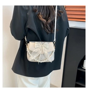 Detail of a creamy white crossbody bag with mesh bow and decorative pearl chain