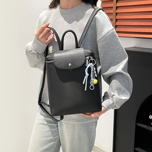 Minimalist black backpack in matte texture with tennis charm accessory on model