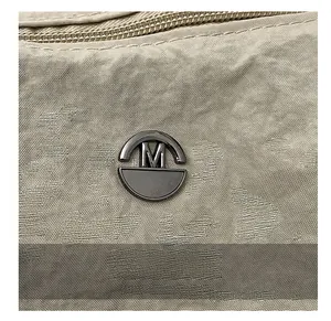 Dettaglio della borsa in tela kaki con logo M metallico e trama della cerniera lampo