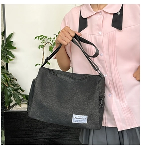 Gros plan du sac bandoulière en toile noire avec étiquette de marque blanche et détails zippés