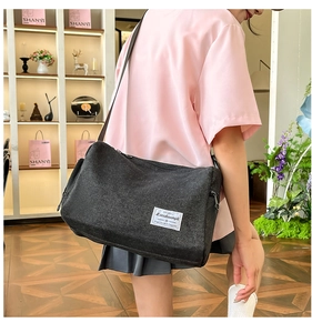 Detail of black textured canvas crossbody bag with adjustable strap and brand label