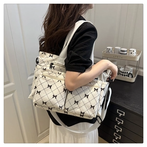 Close-up of cream tote bag featuring black bow patterns and functional zipper pockets