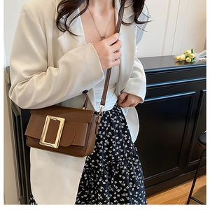 Detail of a brown leather crossbody bag with a vintage gold buckle on a model