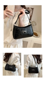 Detail of black faux crocodile leather shoulder bag with silver bow accent and zipper
