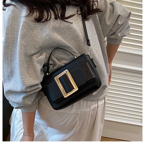 Close-up of black crossbody bag featuring a large decorative gold rectangular buckle