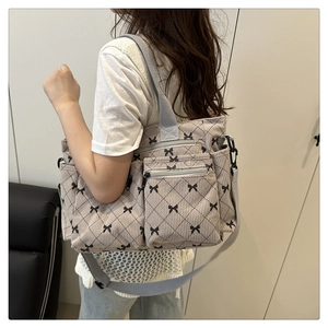 Detail of grey corduroy shoulder bag with black bow pattern and multiple zip pockets
