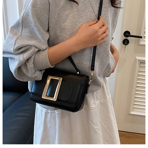 Close-up of black crossbody bag featuring a large gold square buckle and leather texture