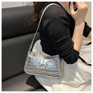 Silver crocodile texture underarm bag with a metallic bow detail worn by a model