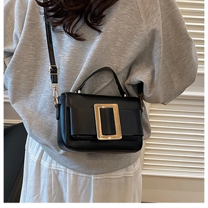 Close-up of black crossbody bag with iconic gold square buckle on a grey sweatshirt