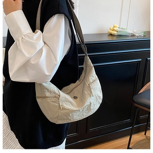 Dettaglio borsa a mezzaluna beige plissettata con doppie cerniere e tracolla ampia