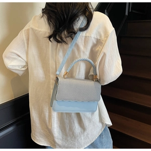 Detail of light blue woven texture bag with wavy flap and braided top handle