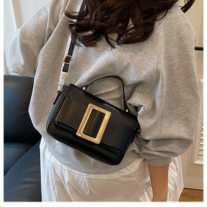 Detail of black glossy leather handbag featuring iconic large gold square metal buckle