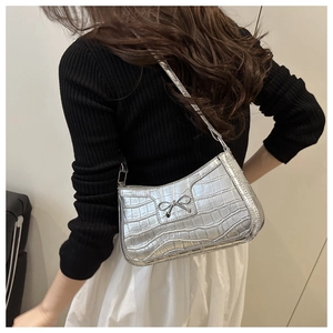 Detailed view of silver crocodile-effect shoulder bag with metal bow and zipper detail