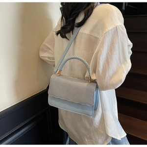 Detail of light blue crossbody bag featuring a wavy woven flap and braided top handle