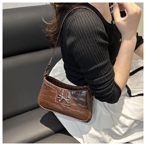 Detailed view of brown crocodile texture leather bag with a silver metal bow accent