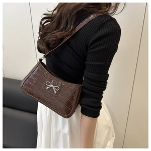 Detail of dark brown crocodile texture shoulder bag with silver bow accent on a model