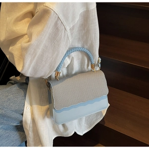 Detail of light blue crossbody bag featuring a woven textured flap and wavy cut edges