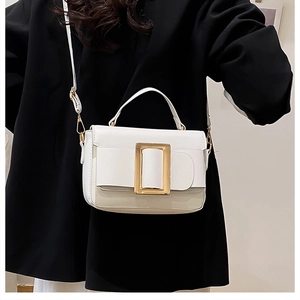 Detailed close-up of a white leather square handbag featuring a large golden metal buckle
