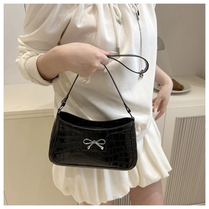 Close-up of black crocodile textured shoulder bag with silver bow buckle on model