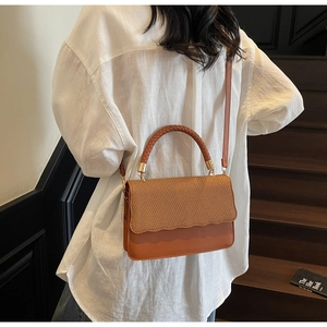 Detail of caramel crossbody bag featuring woven texture flap and wavy edges worn by model