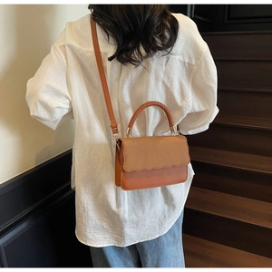 Detail of brown leather crossbody bag featuring woven texture and wavy edge design
