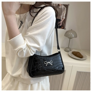 Detail of black faux leather shoulder bag with crocodile texture and silver metal bow