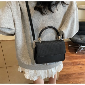Detail of black crossbody bag featuring textured herringbone flap and woven handle strap