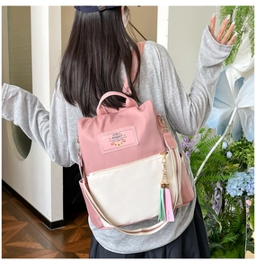 Detail of color-block backpack featuring rabbit tag, fringe tassel and striped strap